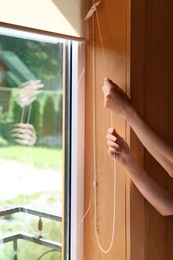 Photo of Young woman opening roller curtains at home, closeup