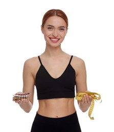 Happy young woman with pills and measuring tape on white background. Weight loss