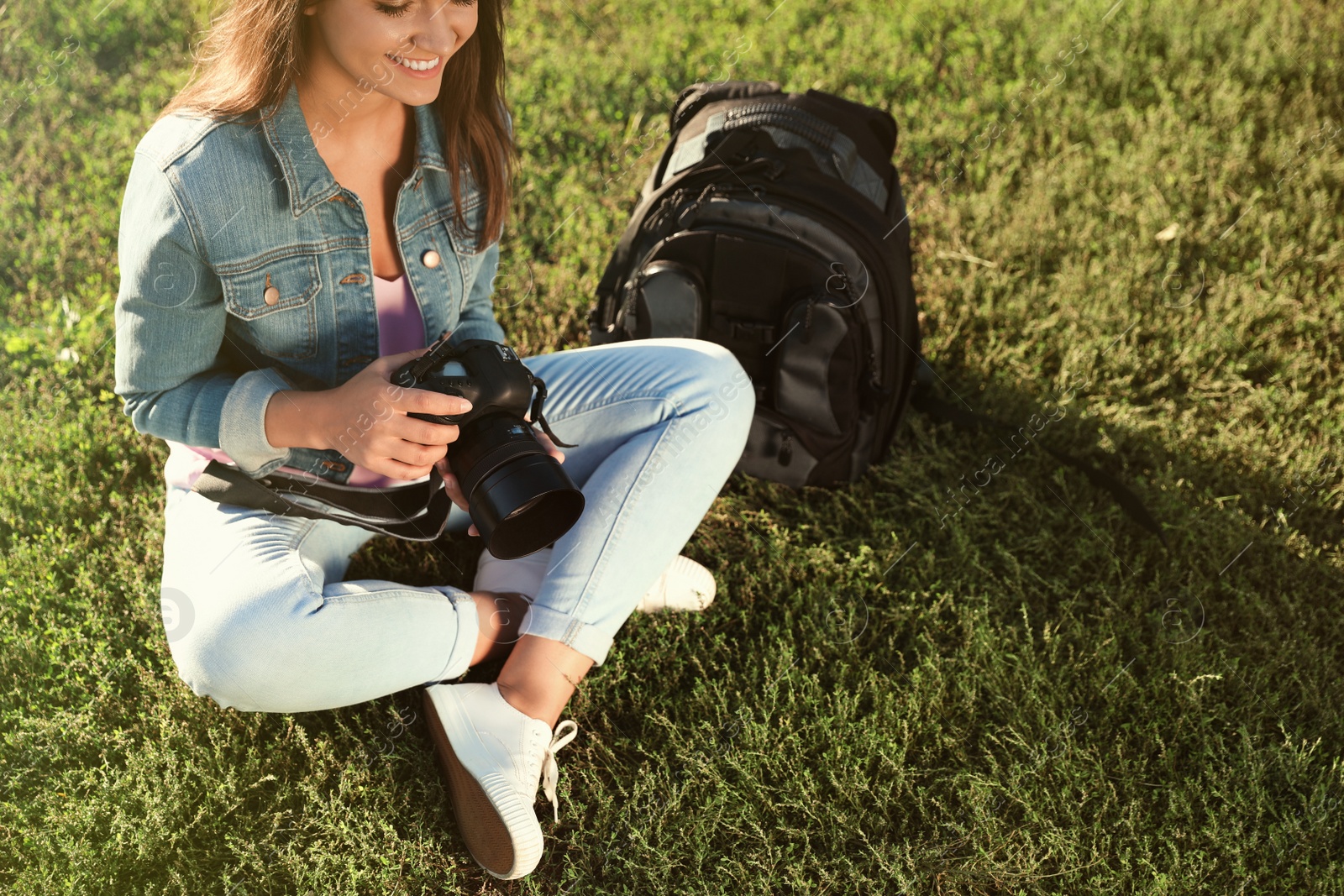 Photo of Young female photographer holding professional camera and sitting on grass outdoors