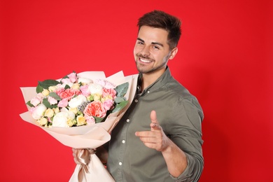 Young handsome man with beautiful flower bouquet on red background