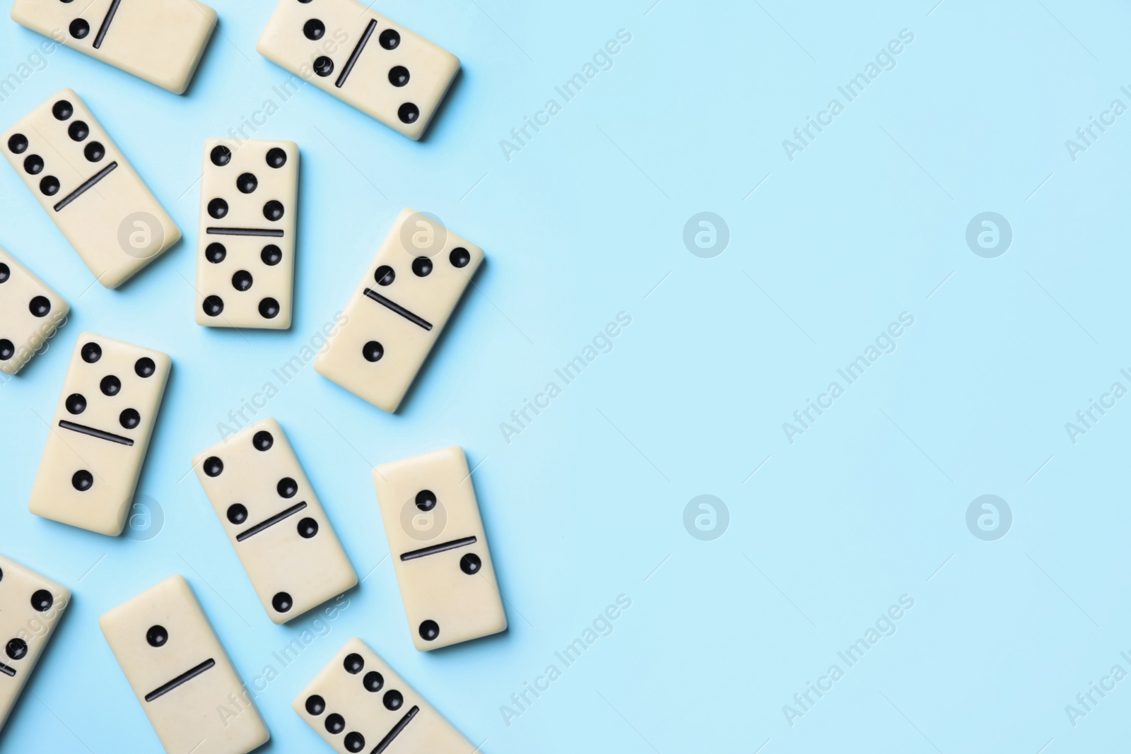 Photo of Classic domino tiles on light blue background, flat lay. Space for text