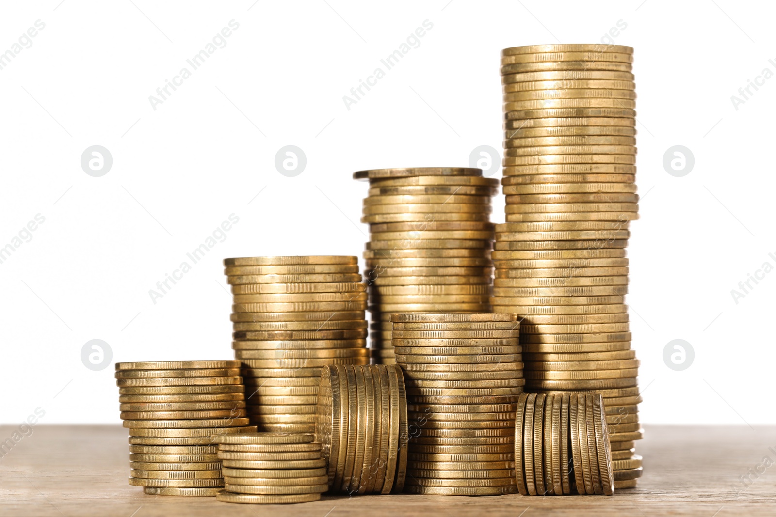 Photo of Many golden coins stacked on wooden table against white background