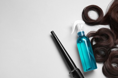 Spray bottle with thermal protection, lock of brown hair and stylish curling iron on light background, flat lay. Space for text
