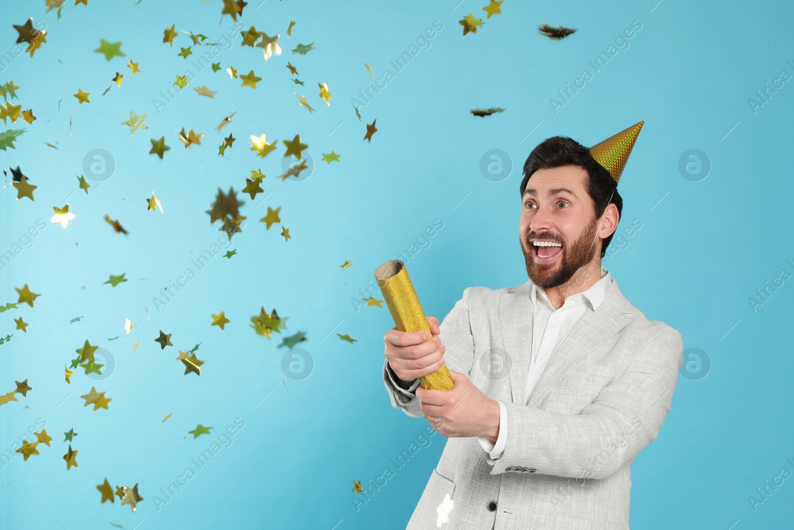 Photo of Emotional man blowing up party popper on light blue background
