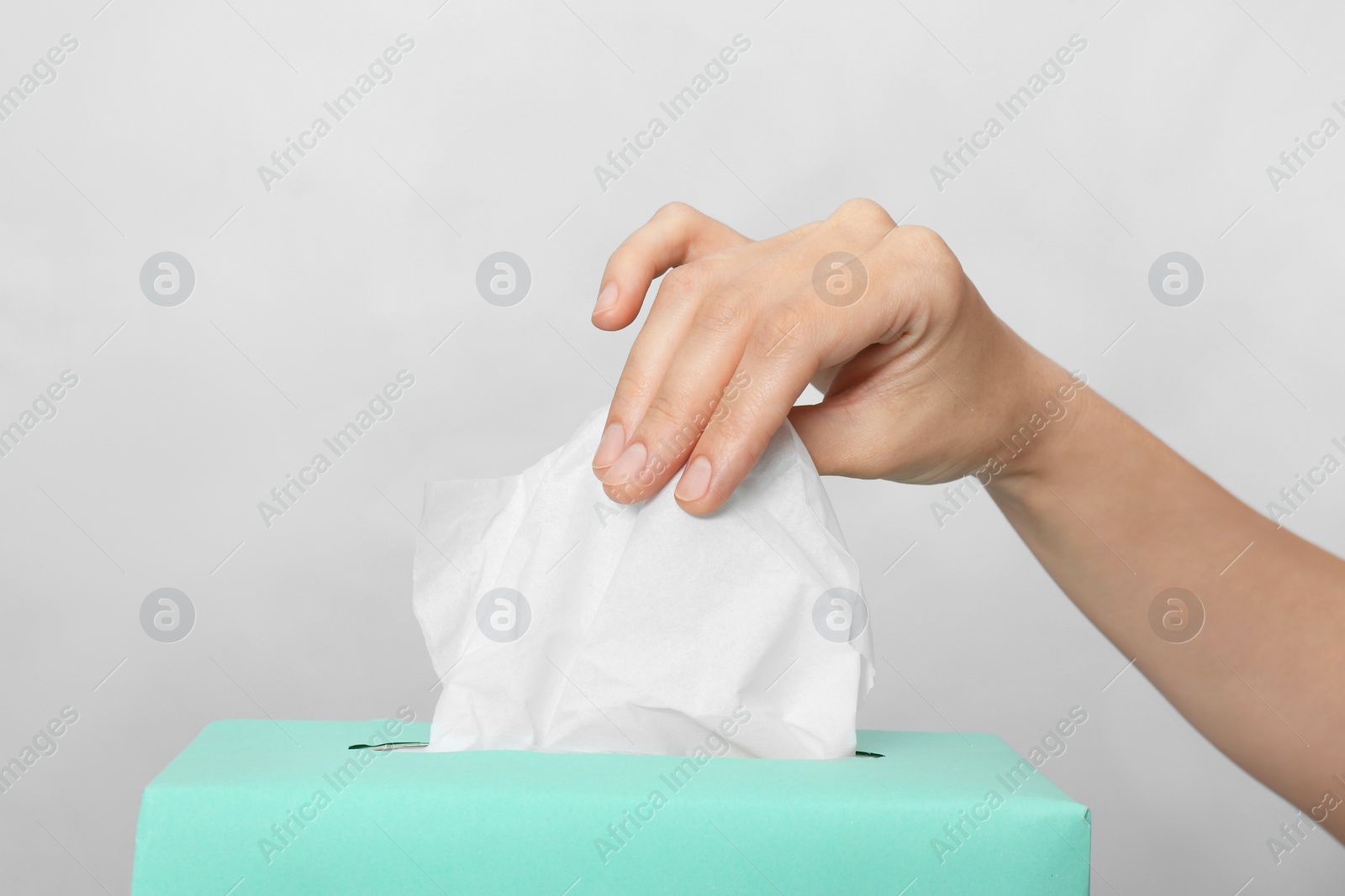 Photo of Woman taking paper tissue from box on light background, closeup