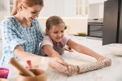 Photo of Mother and daughter rolling dough together in kitchen