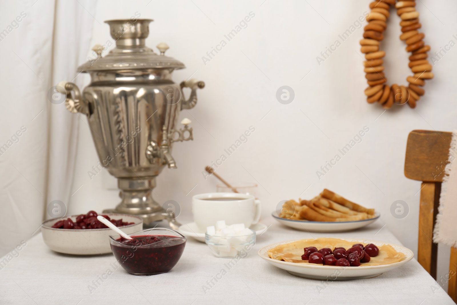 Photo of Vintage samovar, cup of hot drink and snacks served on table indoors. Traditional Russian tea ceremony