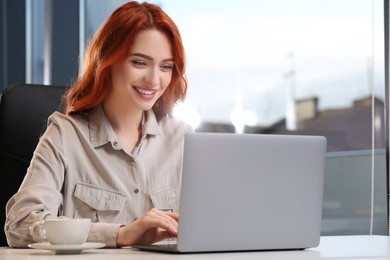 Happy woman working with laptop at white desk in office