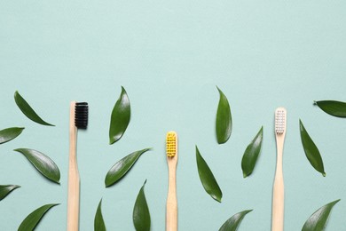 Photo of Toothbrushes and fresh leaves on pale turquoise background, flat lay