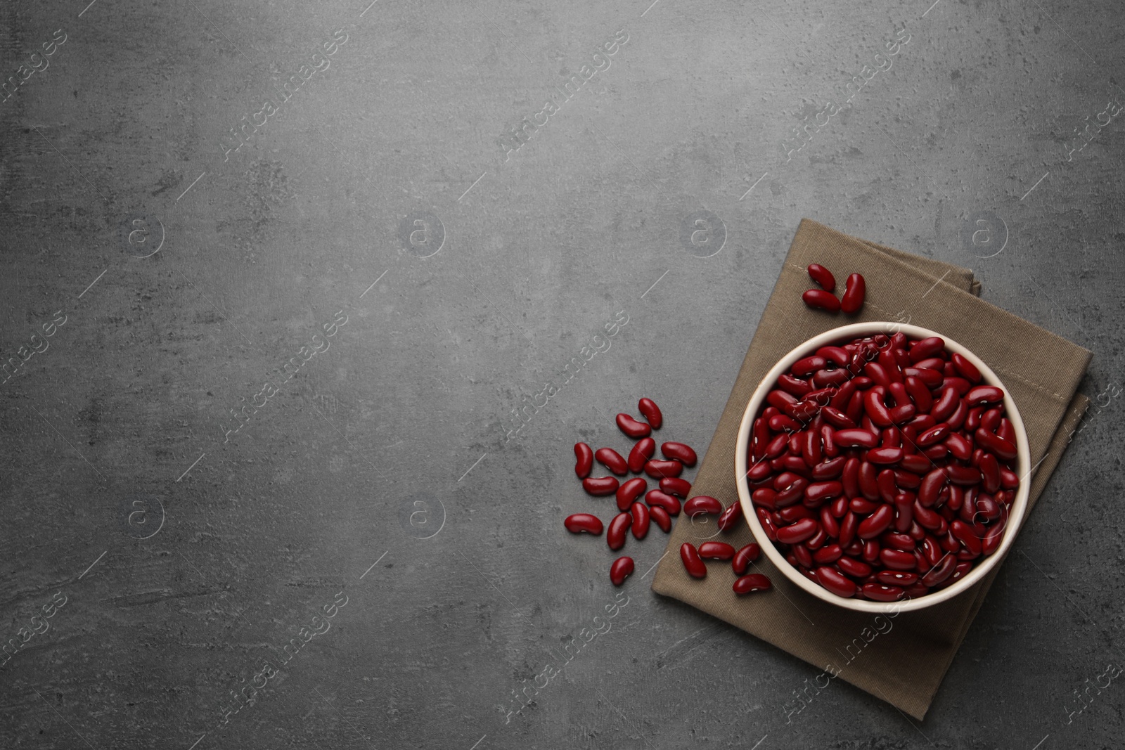 Photo of Raw red kidney beans with bowl and napkin on grey table, flat lay. Space for text