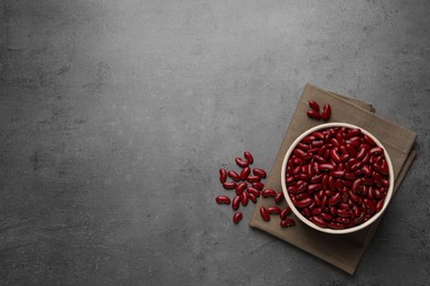 Photo of Raw red kidney beans with bowl and napkin on grey table, flat lay. Space for text