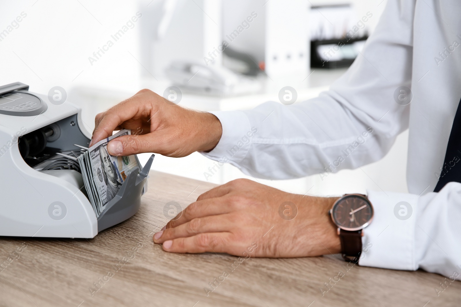 Photo of Male teller putting money into currency counting machine at cash department, closeup