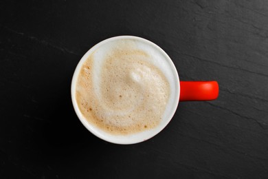 Photo of Red cup with aromatic cappuccino on black textured table, top view