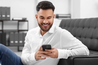 Photo of Handsome young man using smartphone in office