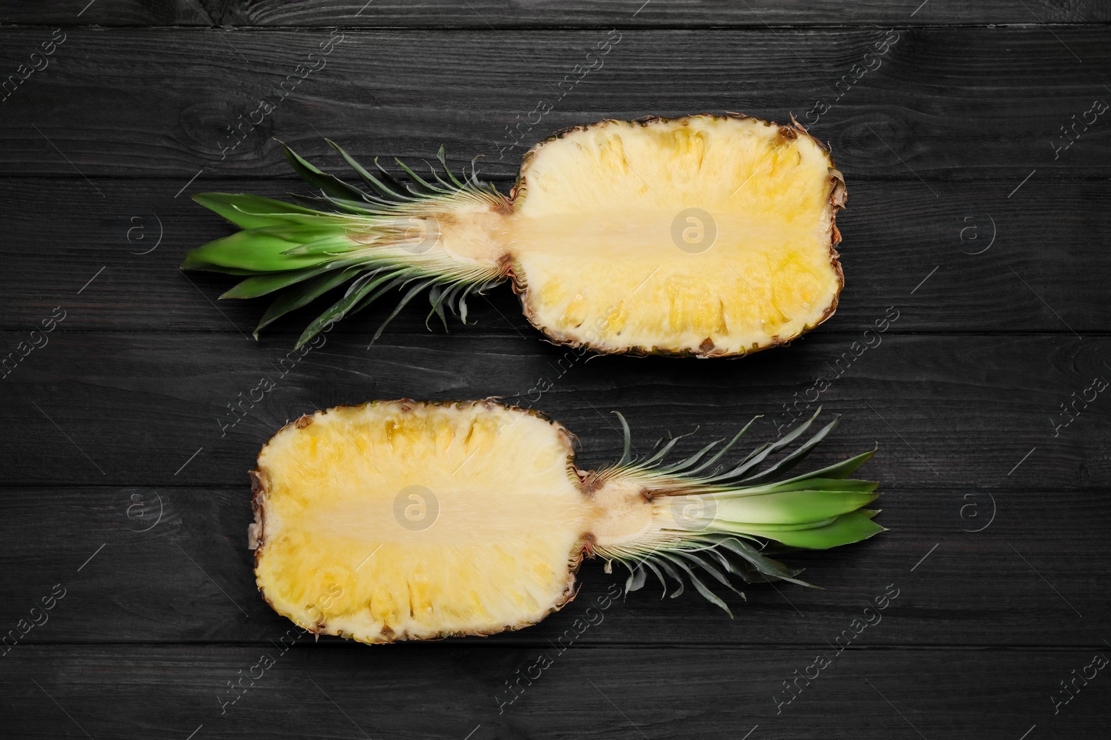 Photo of Halves of ripe juicy pineapple on black wooden table, flat lay