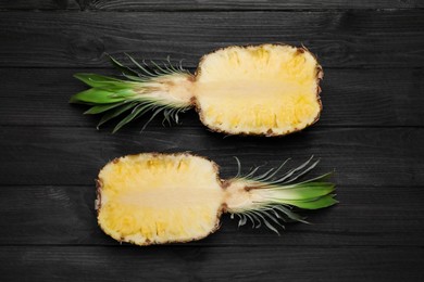 Photo of Halves of ripe juicy pineapple on black wooden table, flat lay