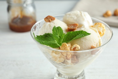 Delicious ice cream with caramel candies and popcorn in dessert bowl on white table, closeup