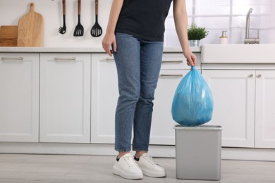 Photo of Woman taking garbage bag out of trash bin in kitchen, closeup