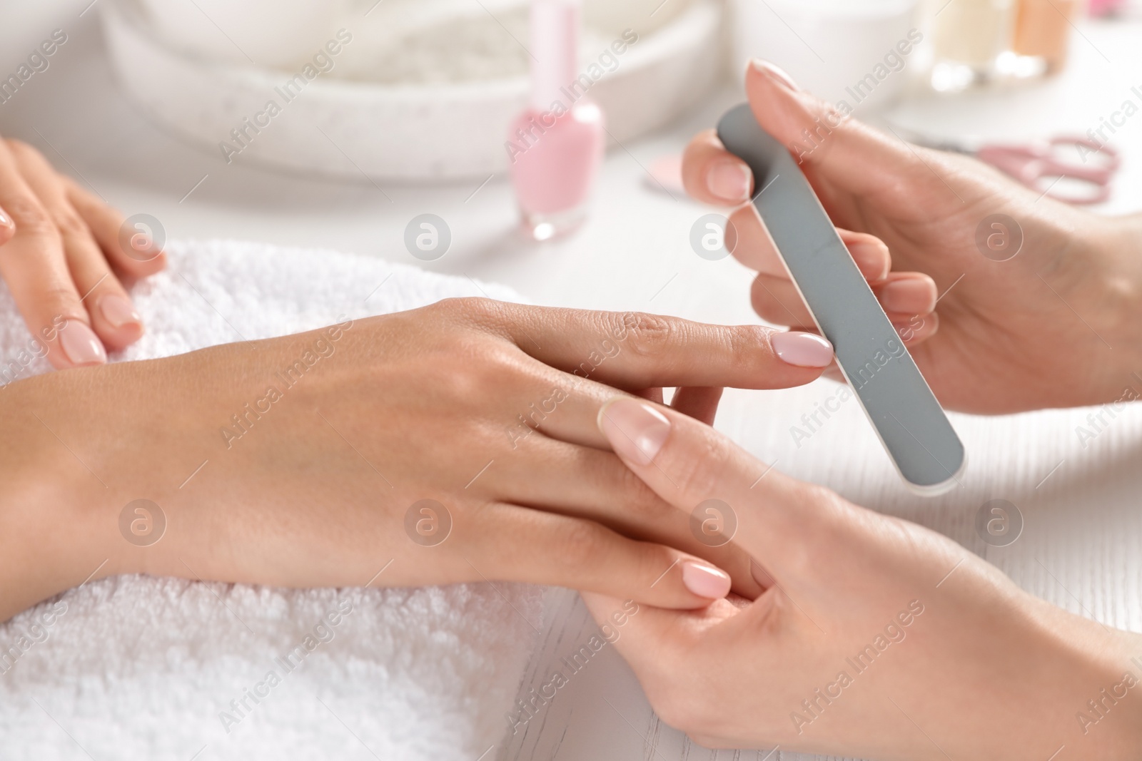 Photo of Manicurist filing client's nails at table, closeup. Spa treatment