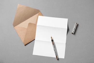 Blank sheet of paper, letter envelope and pen on grey background, top view