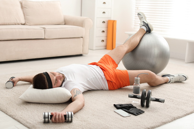 Lazy young man with sport equipment sleeping on floor at home