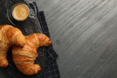 Delicious fresh croissants and cup of coffee on gray table, flat lay. Space for text