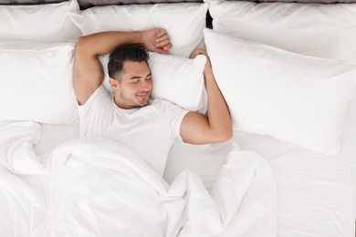 Photo of Young man sleeping in bed with soft pillows at home, top view