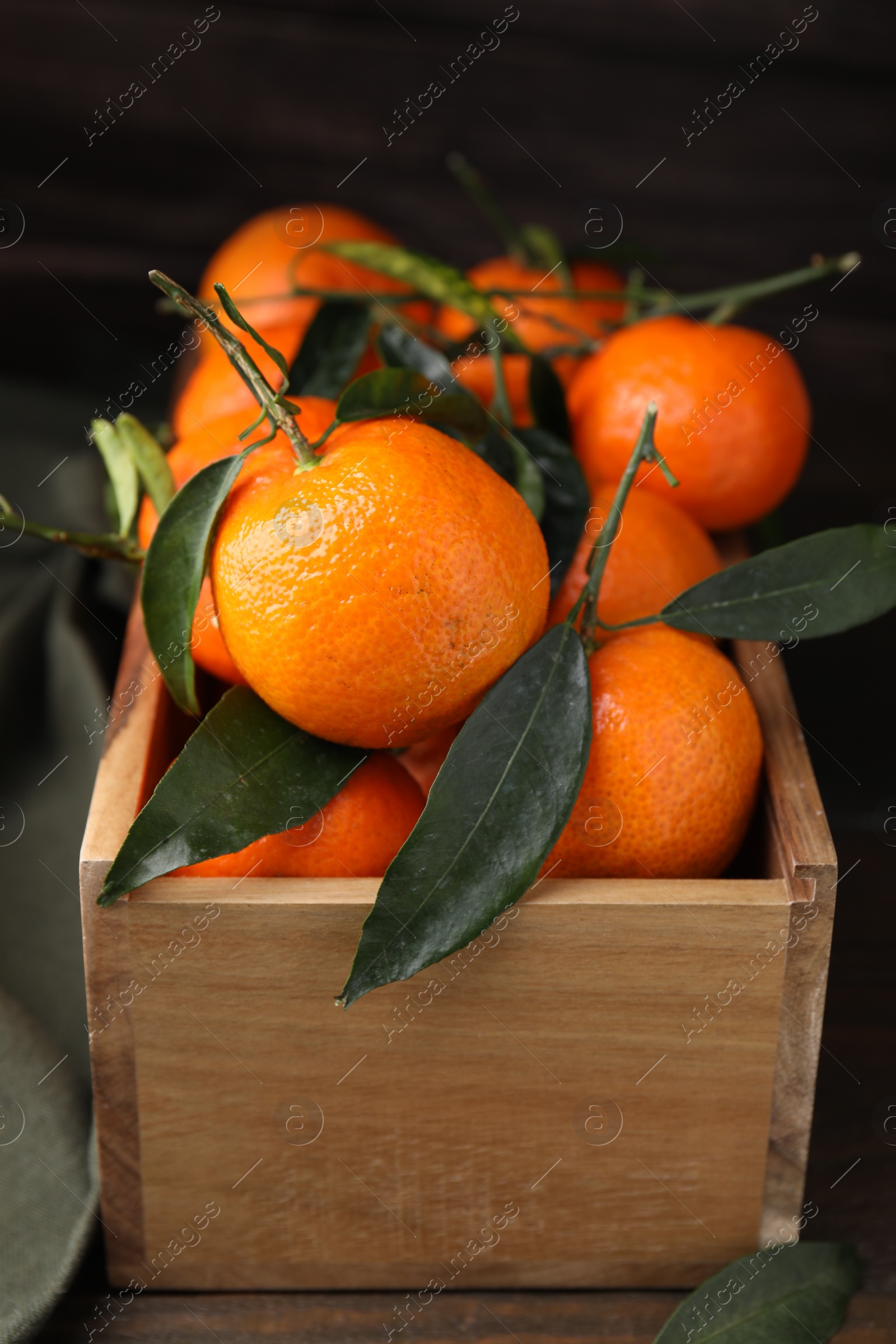 Photo of Crate with fresh ripe tangerines and leaves on wooden table, closeup