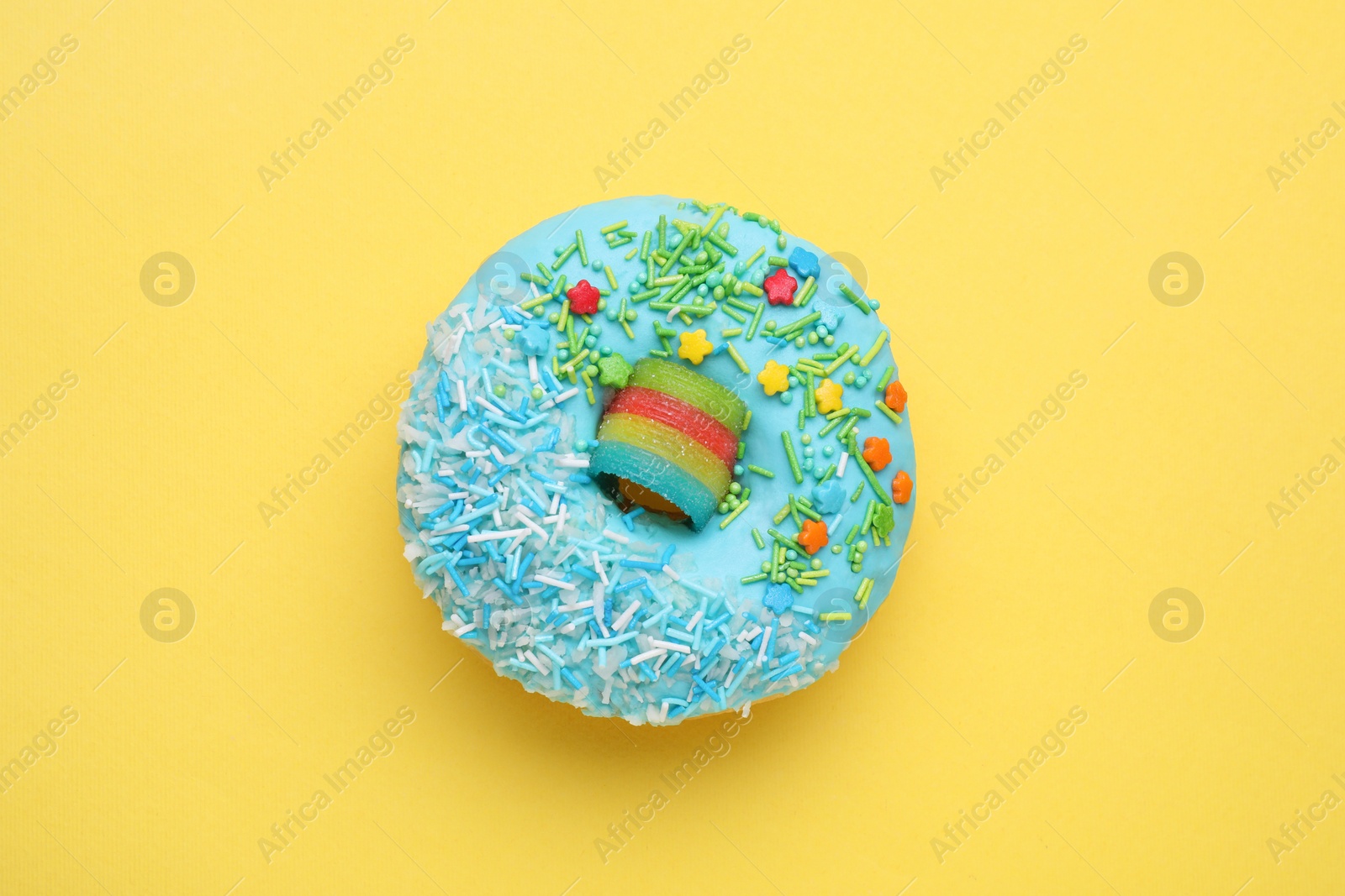 Photo of Glazed donut decorated with sprinkles on yellow background, top view. Tasty confectionery