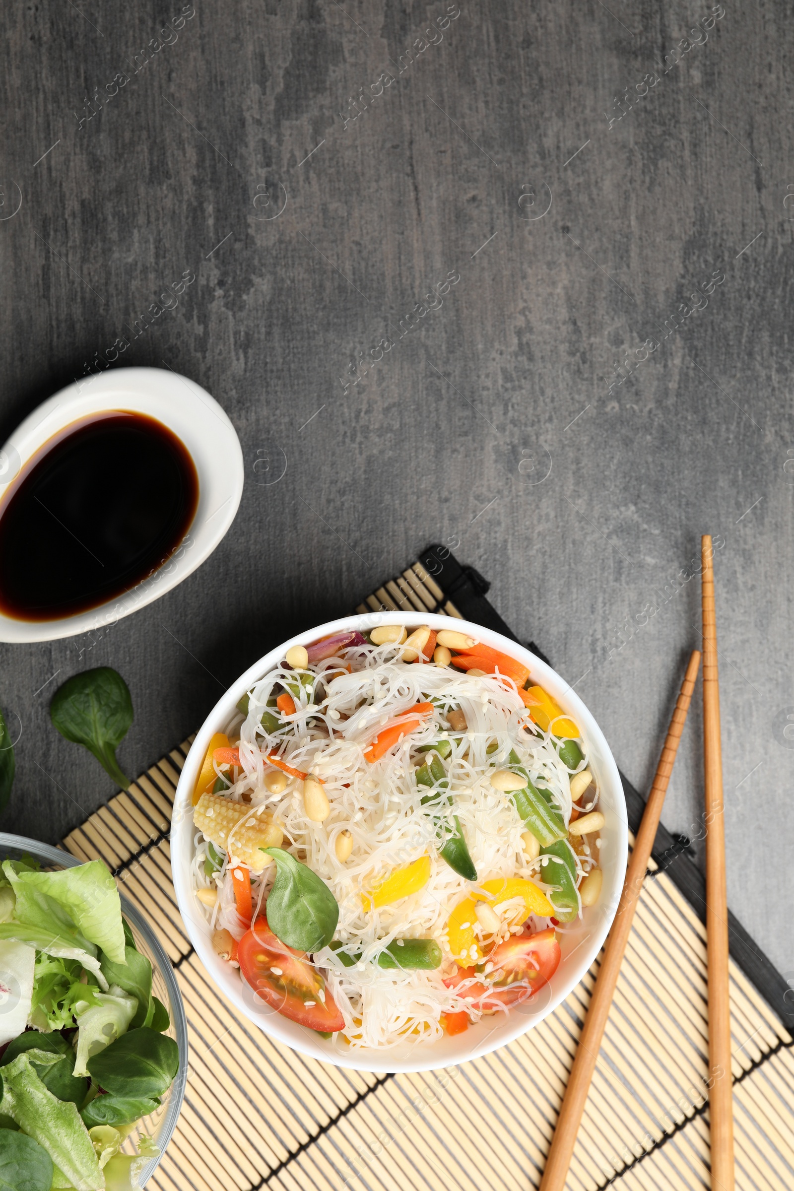 Photo of Tasty cooked rice noodles with vegetables served on grey table, flat lay. Space for text
