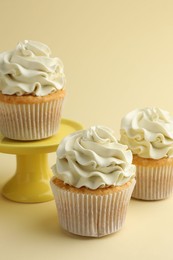 Photo of Tasty vanilla cupcakes with cream on pale yellow background, closeup