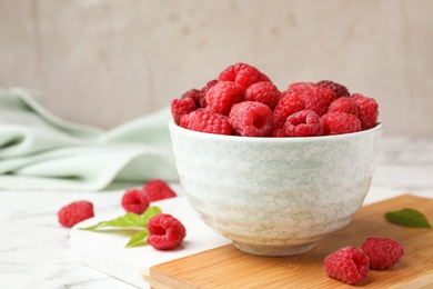 Bowl with delicious ripe raspberries on cutting board against light background, space for text