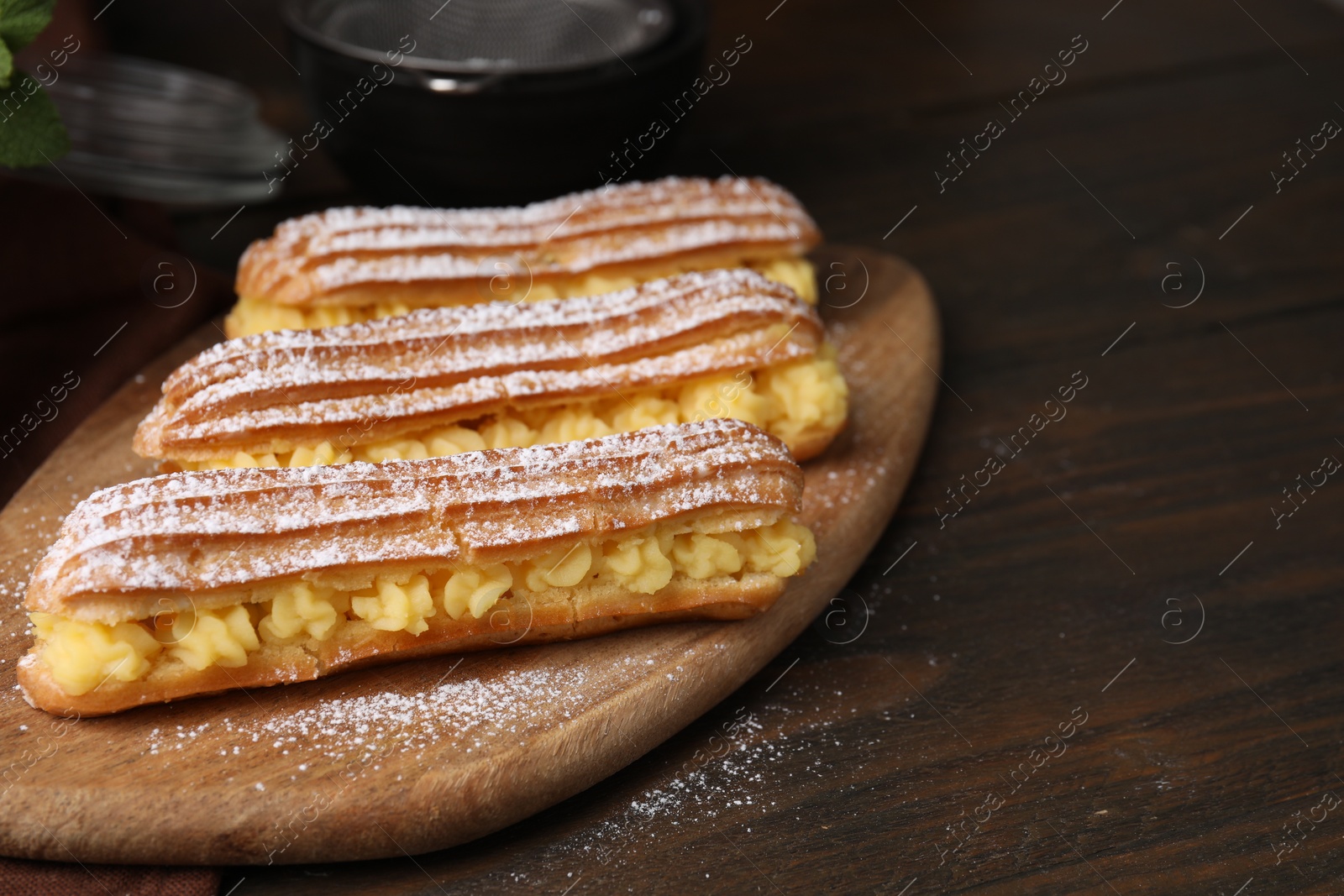 Photo of Delicious eclairs filled with cream on wooden table, space for text