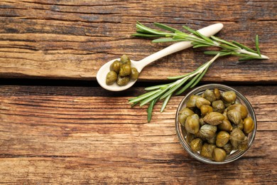 Photo of Tasty capers, rosemary and spoon on wooden table, flat lay. Space for text