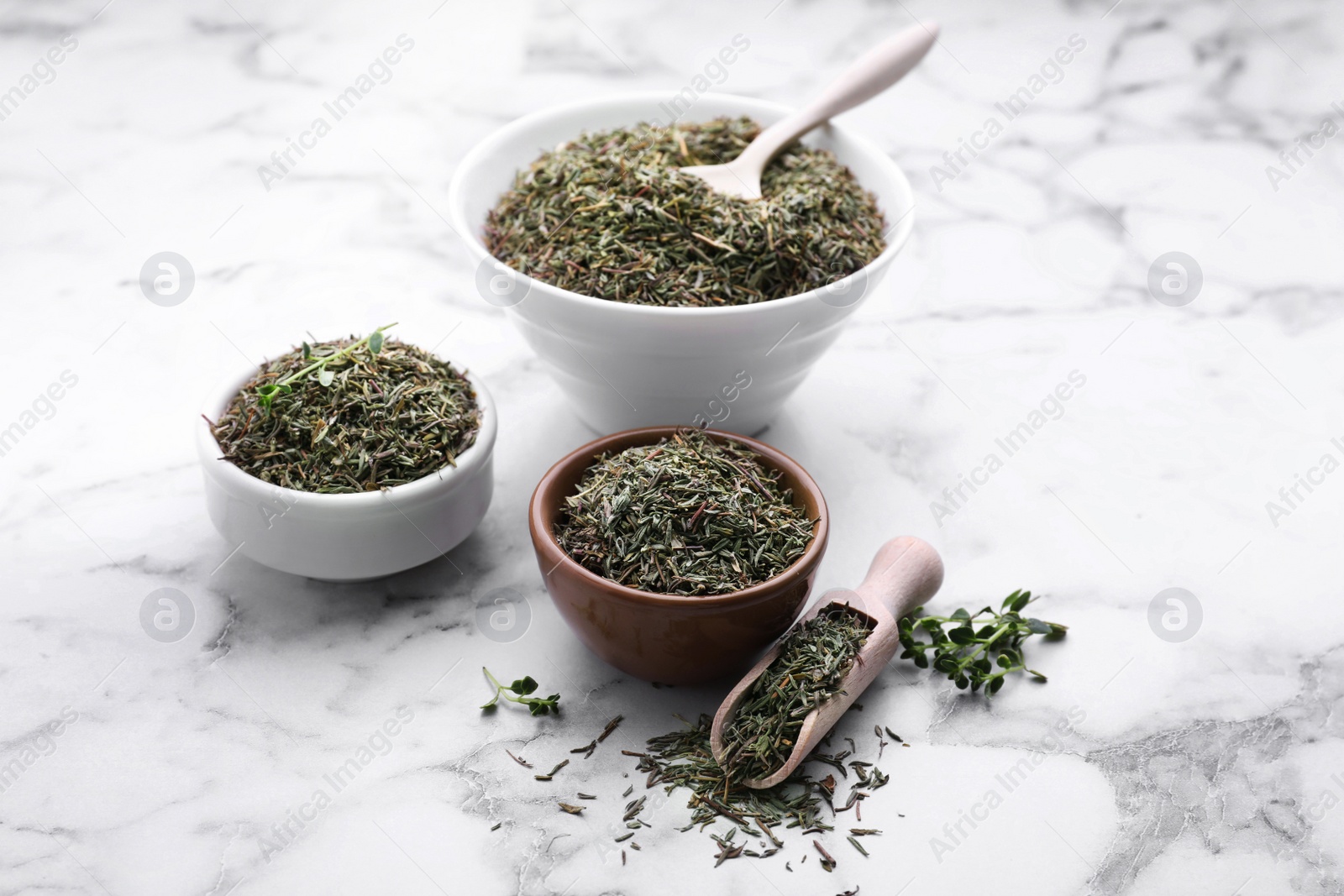 Photo of Bowls, scoop and spoon with dried thyme on white marble table