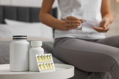 Photo of Woman holding glass of water, focus on table with pills in room. Weight loss