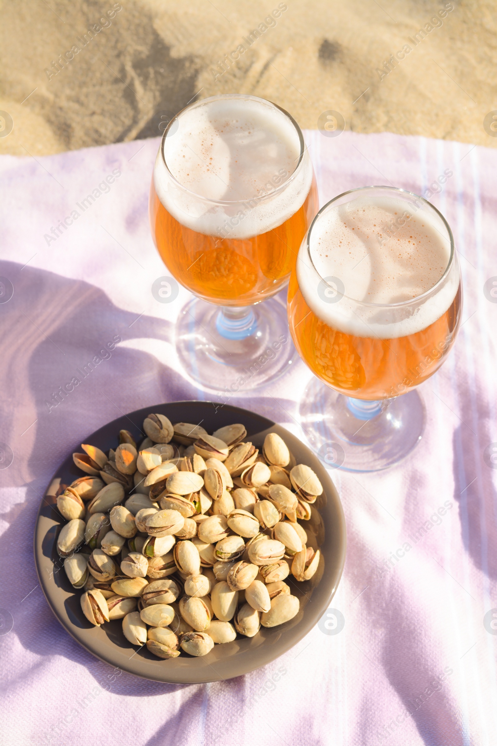 Photo of Glasses of cold beer and pistachios on sandy beach, above view