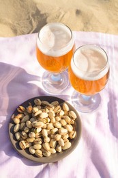 Glasses of cold beer and pistachios on sandy beach, above view