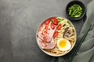 Delicious ramen in bowl served on grey textured table, flat lay and space for text. Noodle soup