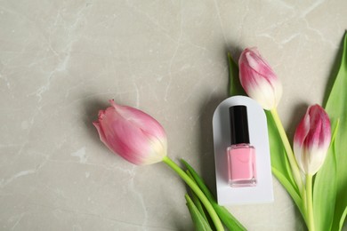 Flat lay composition with pink nail polish in bottle and tulip flowers on light textured table. Space for text