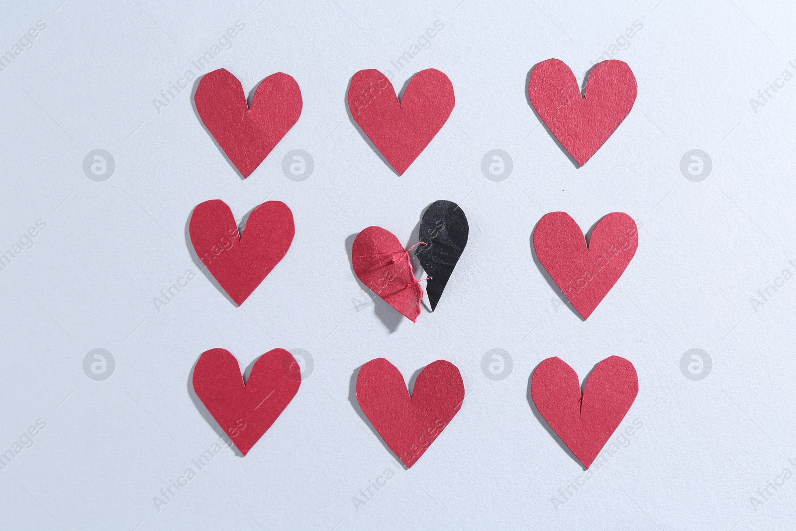 Photo of Halves of torn paper heart connected by thread and red decorative hearts on gray background, flat lay. Relationship problem concept