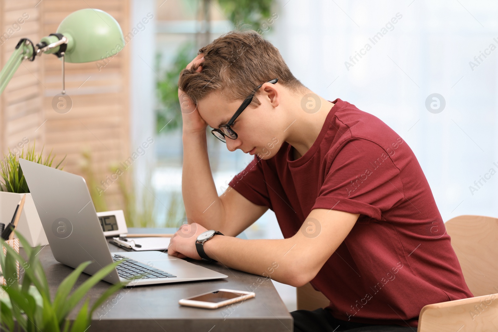 Photo of Troubled teenage boy with laptop at table in room
