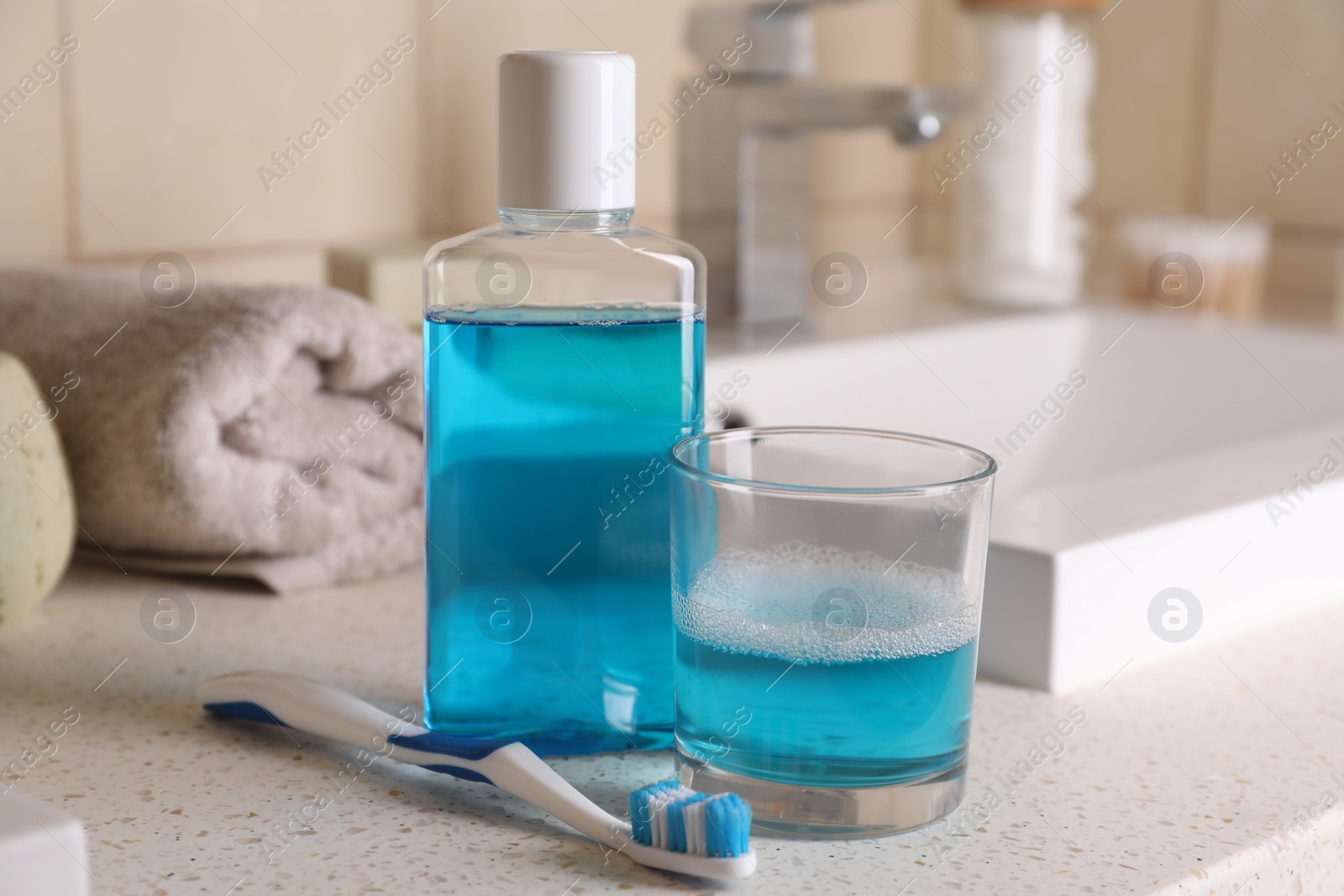 Photo of Fresh mouthwash in bottle, glass and dental floss on countertop in bathroom, closeup