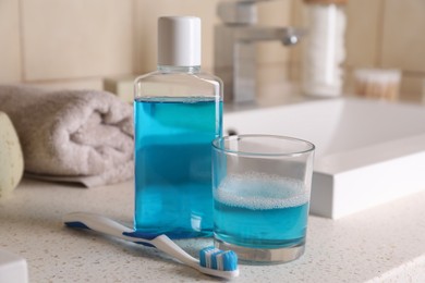 Photo of Fresh mouthwash in bottle, glass and dental floss on countertop in bathroom, closeup