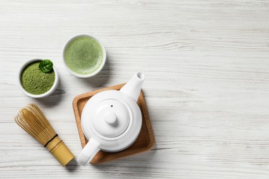 Photo of Cup of fresh matcha tea, bamboo whisk, teapot and green powder on white wooden table, flat lay. Space for text