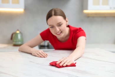 Photo of Woman cleaning white marble table with rag in kitchen, selective focus