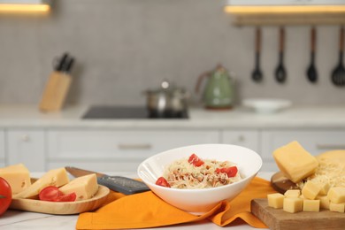 Photo of Delicious pasta with grated cheese and tomatoes on white table in kitchen