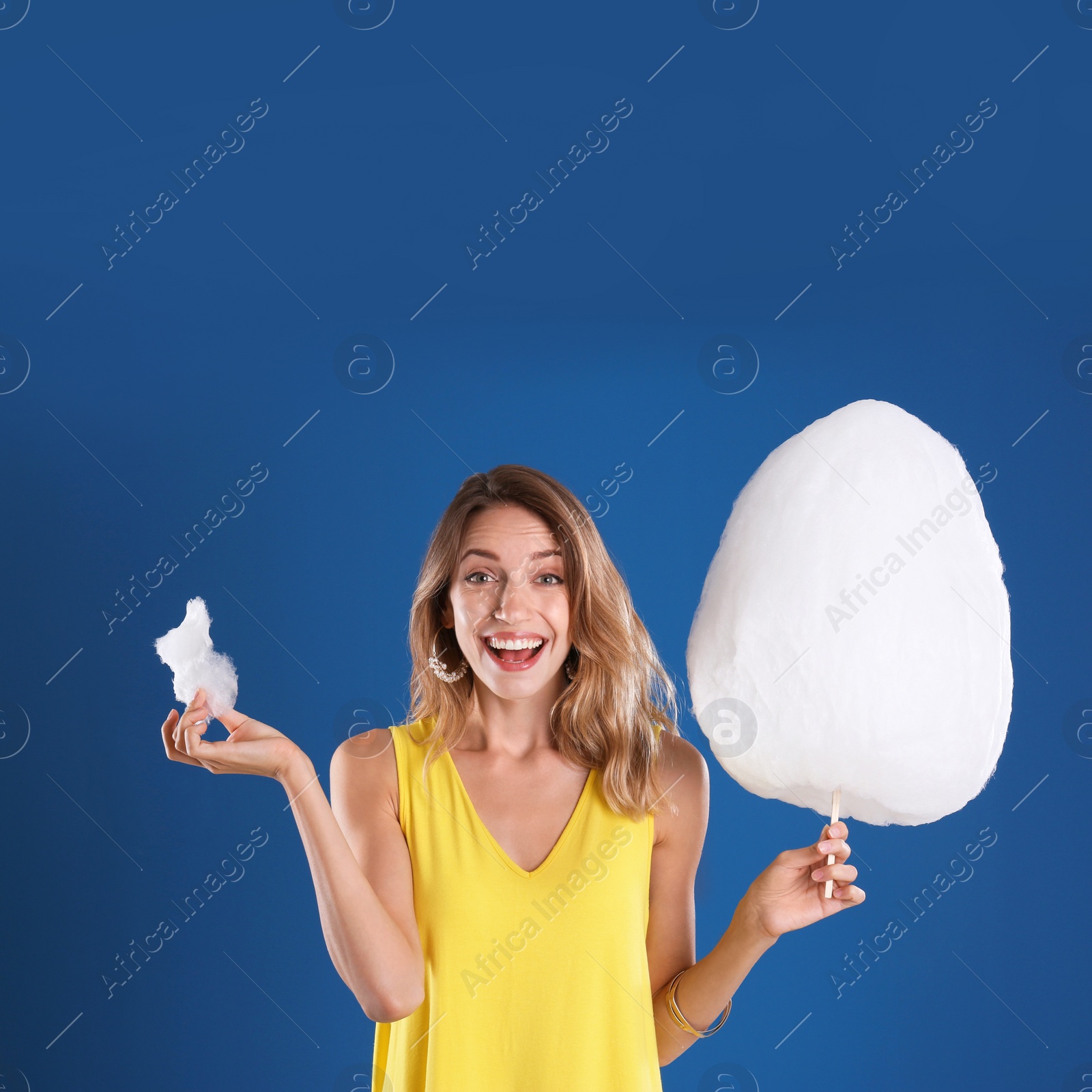 Photo of Happy young woman with cotton candy on blue background