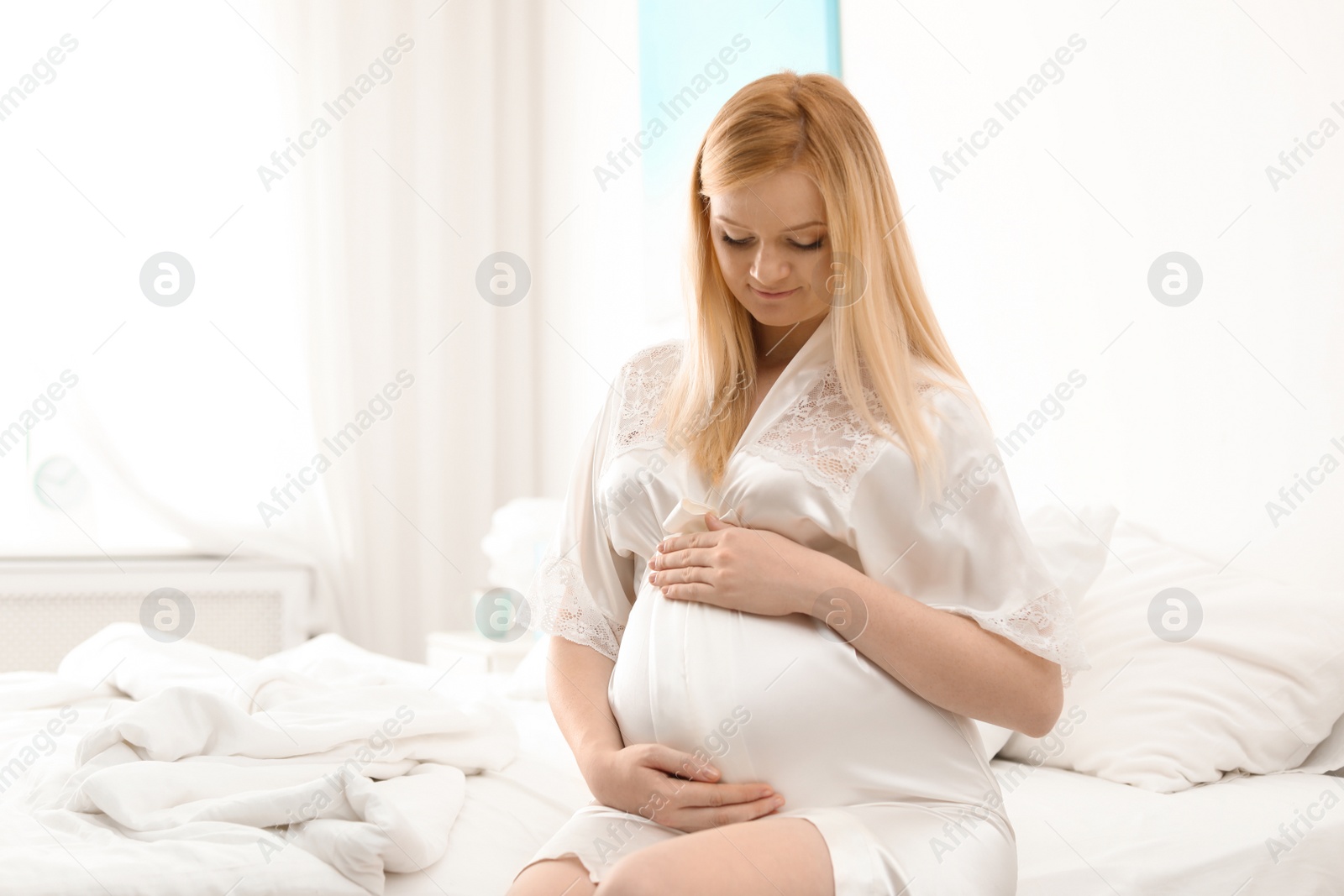 Photo of Beautiful pregnant woman sitting on bed in light room