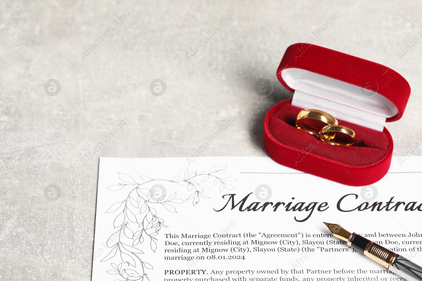 Photo of Marriage contract, fountain pen and golden wedding rings on grey table